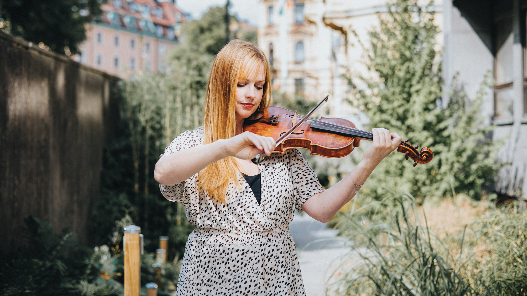 Hannah Sundkvist spelandes på sin fiol. I bakgrunds finns grönska och husgavlar. foto Tess Wallenberg
