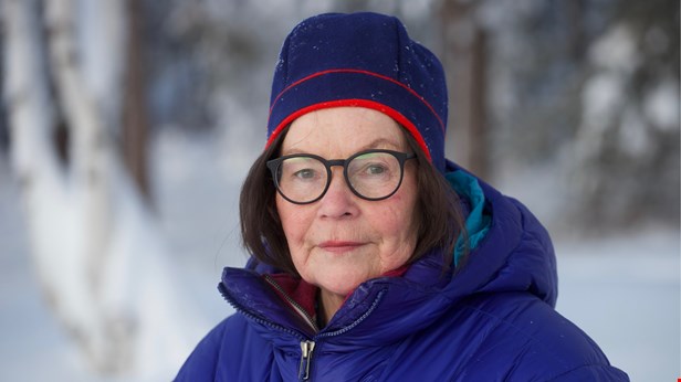 Karin Tuolja står utomhus och tittar in i kameran. På sig har hon en blå mössa och jacka.