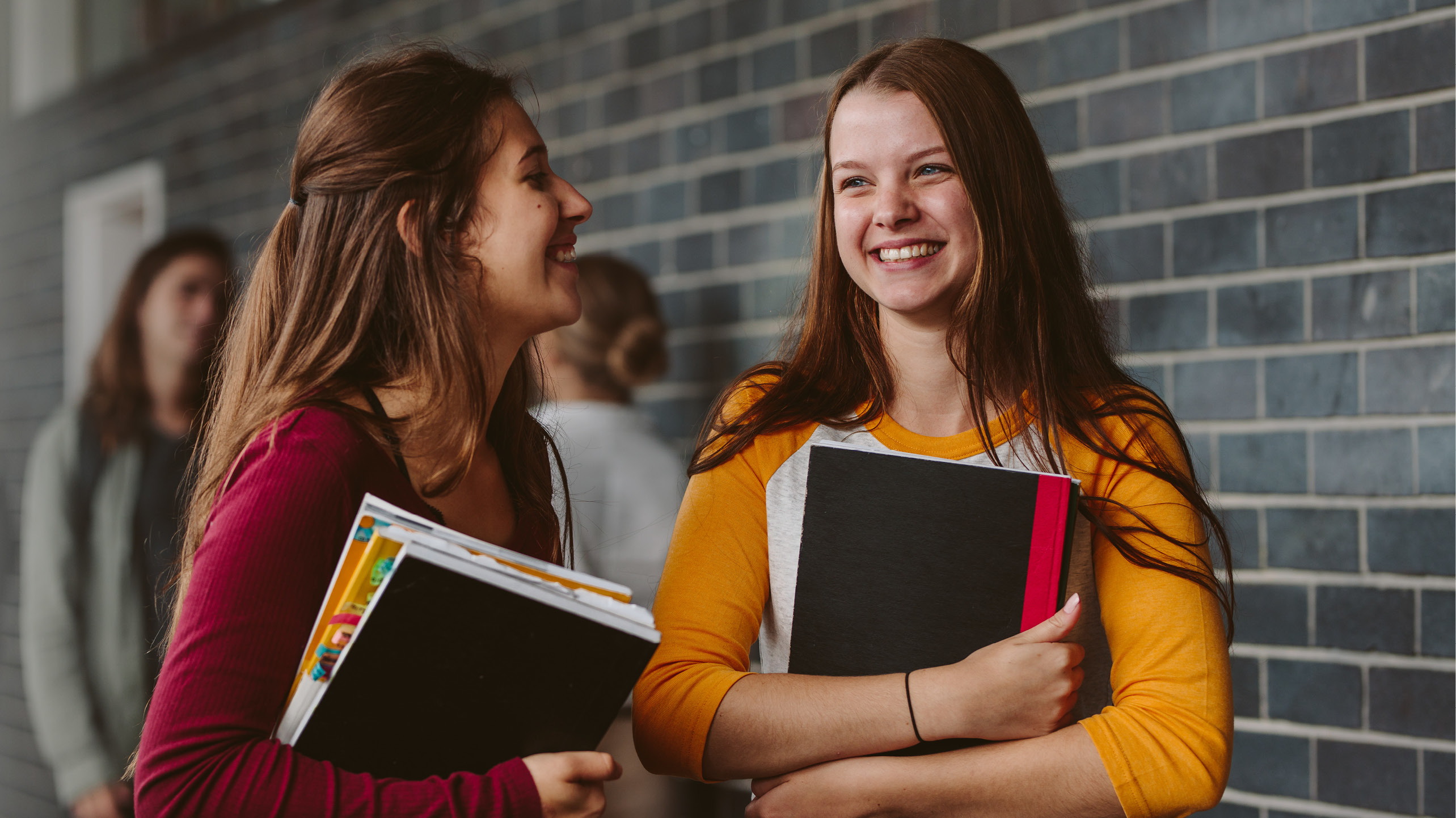 Två glada flickor i tonåren med böcker i famnen, som går i en skolkorridor, foto Istock