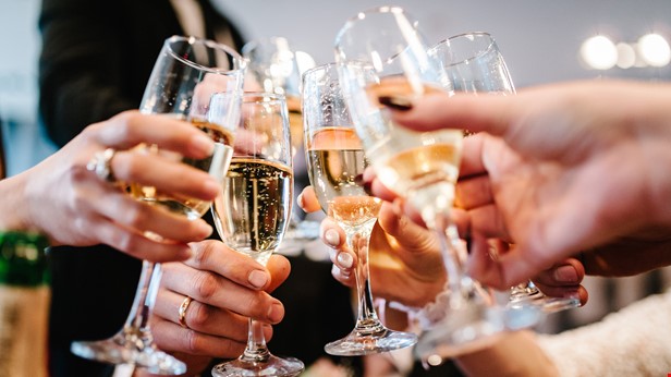 Händer håller i höga glas. Foto Istock