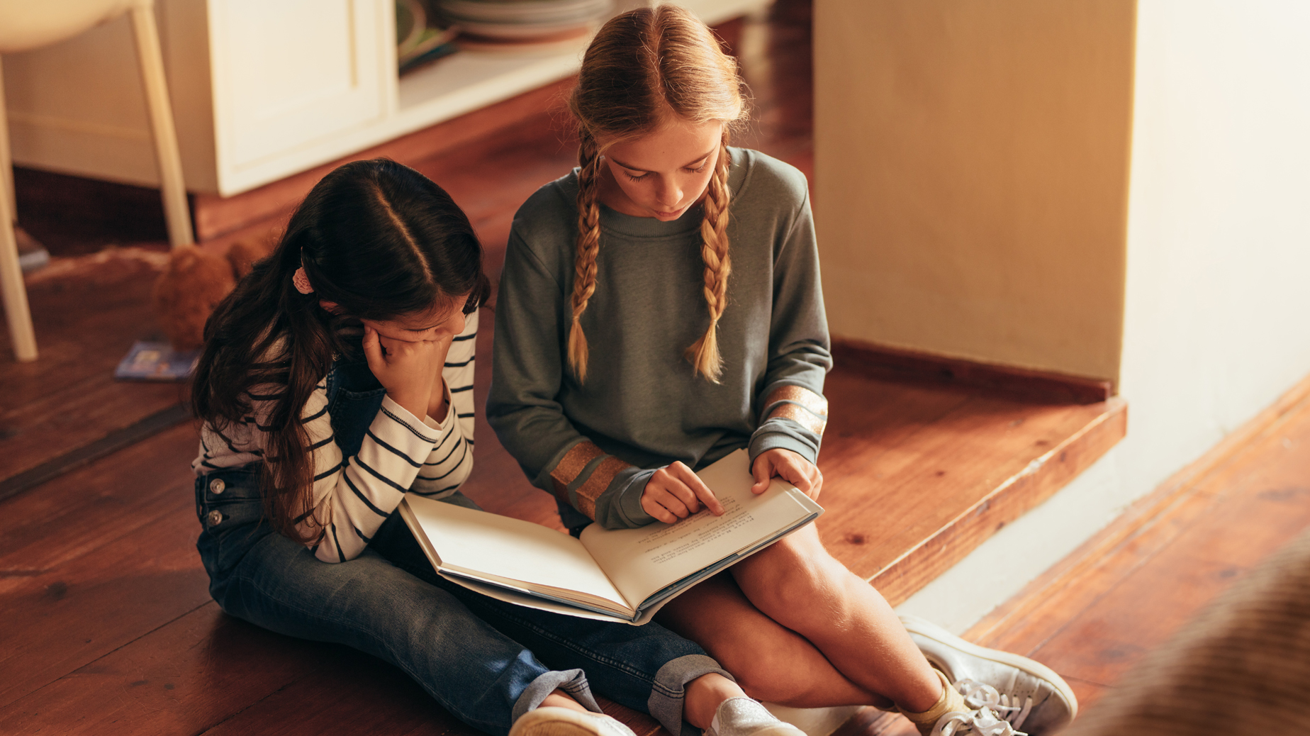 Två flickor sitter och håller en uppslagen bok framför sig. Foto Istock