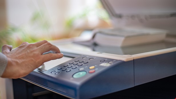 Person står vid en kopiator och har handen på den, foto Istock