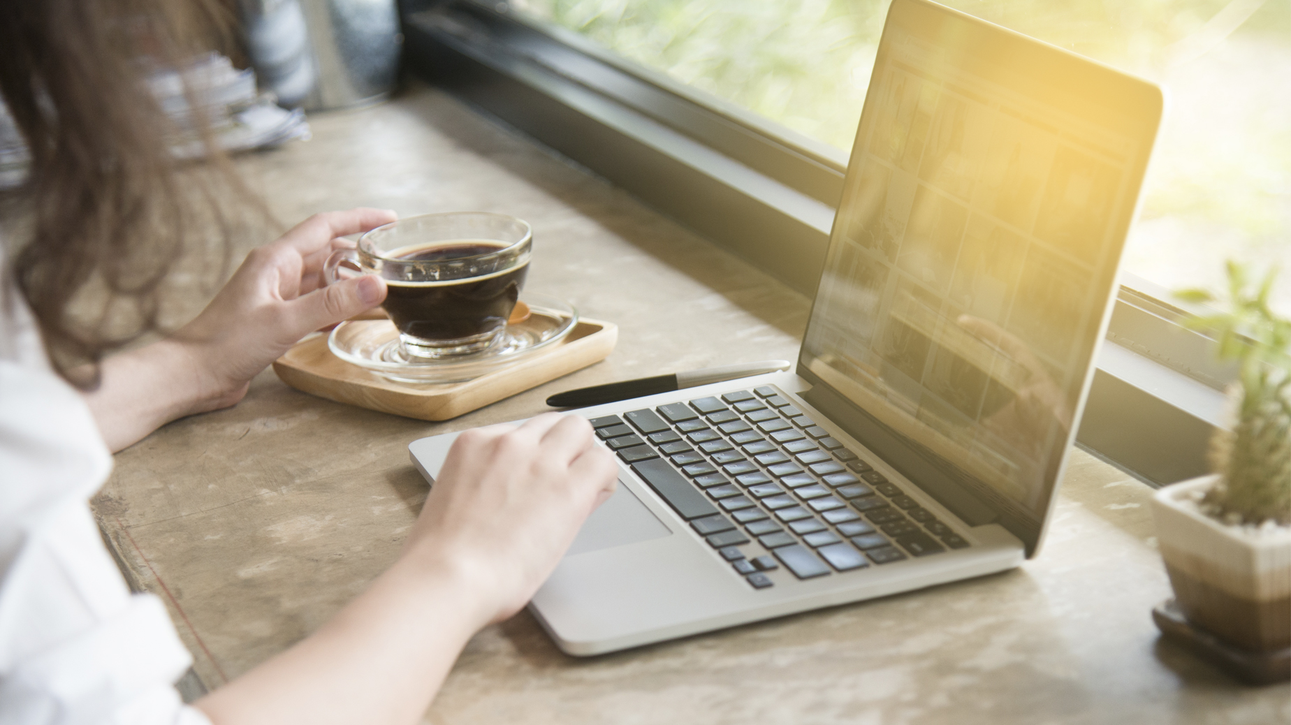 Kvinna med händer på en laptop som ligger på ett bord. Bredvid står en kopp med mörkt dryck. Foto Istock