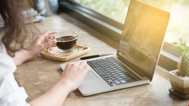 Händer på tangentbordet på en laptop. En kopp bredvid.Solen skiner in genom fönstret. Foto Istock