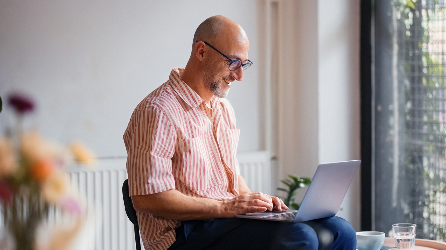 Man sitter med laptop i knä, han ler. Foto: Istock